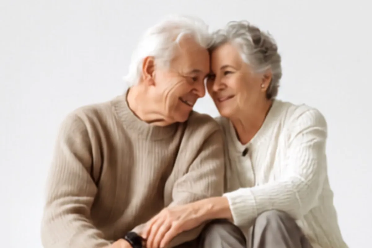 An elderly couple sitting close together, smiling warmly at each other